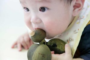 赤ちゃんが出産祝いの木のおもちゃのガラガラを口に入れて遊んでいる