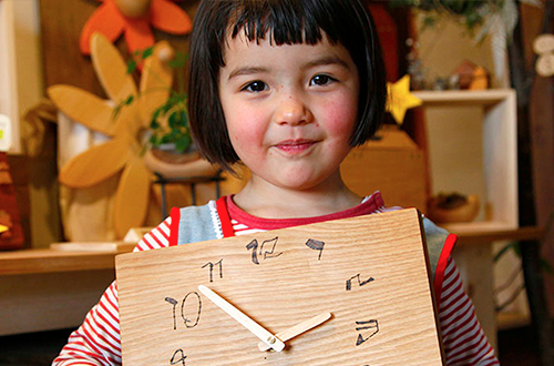 記念の贈り物 女の子が木の時計を持っている。自分の字の数字になっている時計。