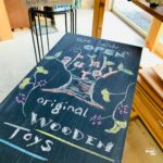 木のおもちゃ工房のスタッフが手描きで看板を描いている様子。木のぬくもりとクラフト感を伝える