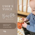 赤ちゃんが京都の工房で作られた木のガラガラを手に持って遊ぶ様子。やさしい木の色と温かみのあるデザイン。