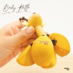 手に持った木製の赤ちゃんガラガラ。丸みのあるパーツとやさしい色合いで、工房で製作された様子が伝わる写真。