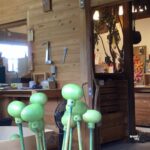 木工房の中で、緑色に塗装された赤ちゃんガラガラ「かえるちゃん」のパーツが乾燥されている制作途中の様子