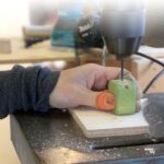 工房で職人が木製ひも通しおもちゃに穴あけ加工をしている制作風景