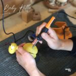 工房で焼きペンを使い、木製の赤ちゃんガラガラに名前を名入れしている作業風景