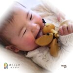 きりんの形をした木のガラガラを手にして遊ぶ赤ちゃん。春の出産祝いに人気の名入れ対応木製おもちゃ。