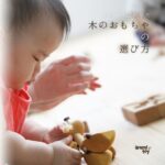 赤ちゃんが木のおもちゃを手に取り、集中して遊んでいる様子。手の動きや興味を大切にしたおもちゃ選びのイメージ。